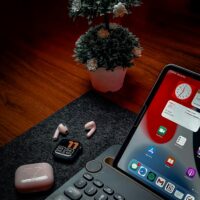 A stylish desktop setup featuring an iPad, keyboard, earbuds, and decorative plant.