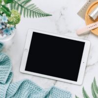 Flat lay of technology with tablet, watch, and plants on marble surface.