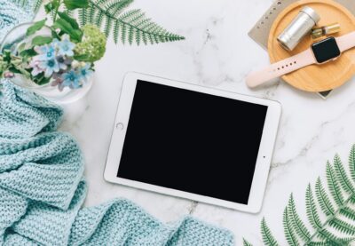 Flat lay of technology with tablet, watch, and plants on marble surface.