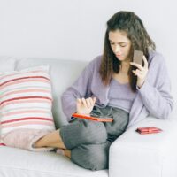 Woman sitting on a couch enjoying online shopping with a digital device and credit card.